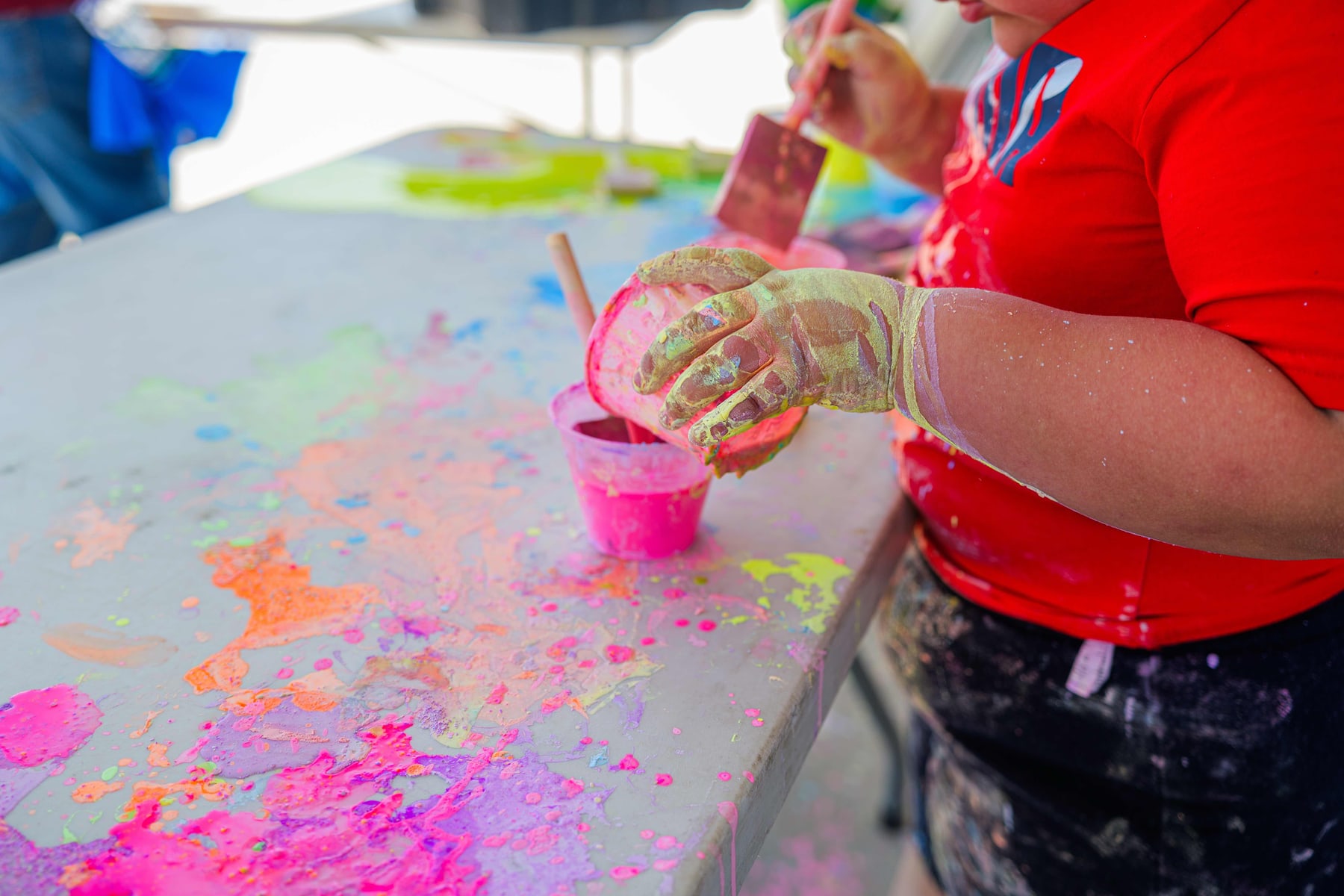 Hands mixing bright paint at a Ganas craft table