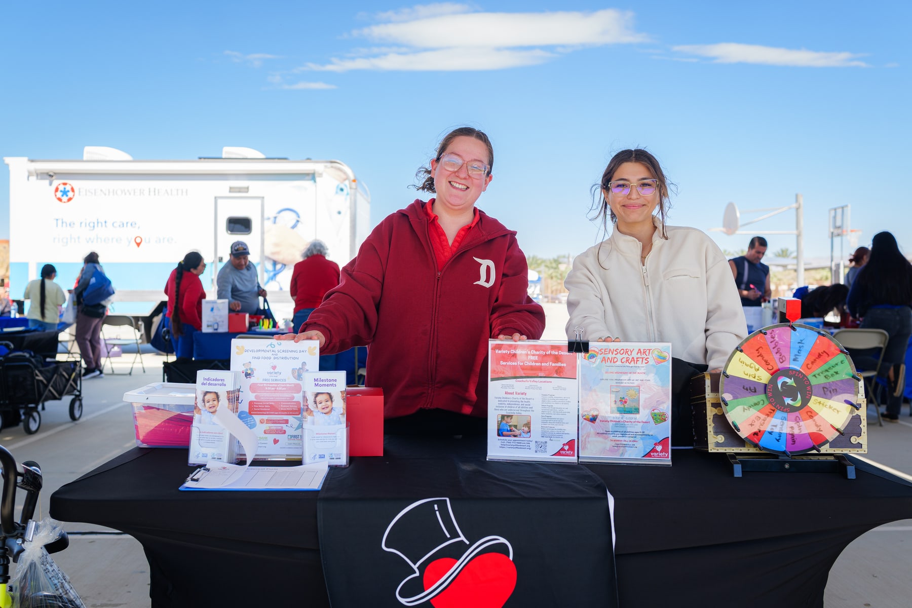 Two volunteers at an outreach table with flyers and a prize wheel