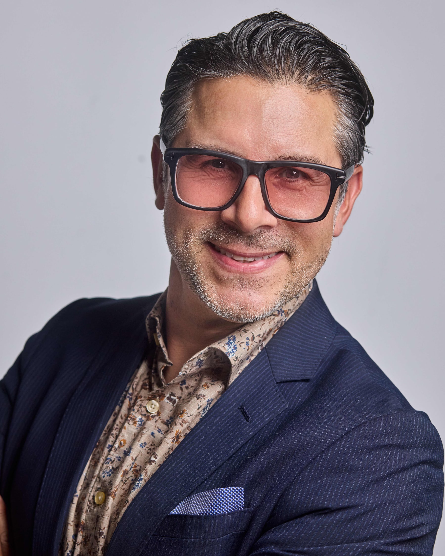 Studio headshot of a man in a patterned shirt and navy jacket