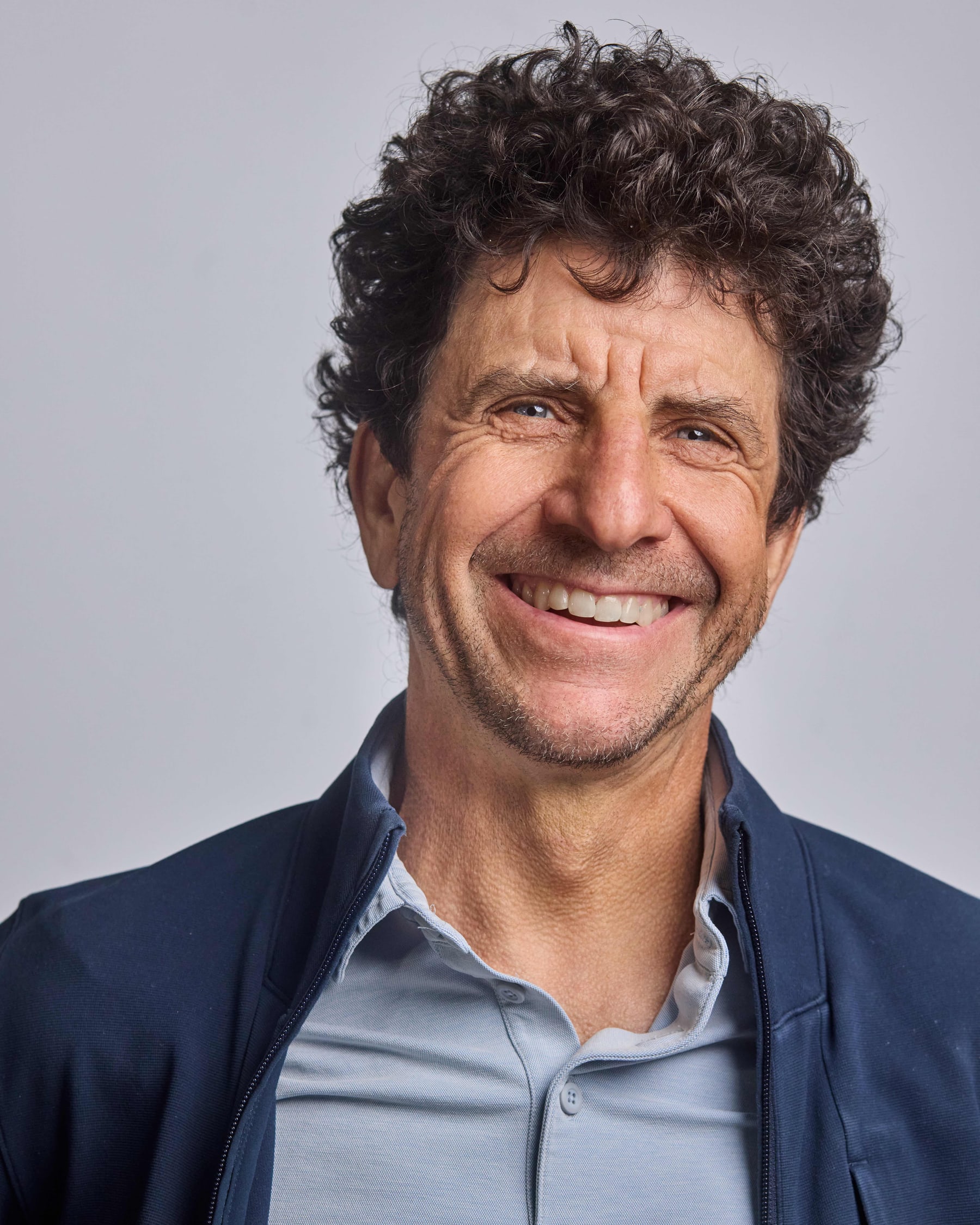 Studio headshot of a man with curly hair in a blue jacket