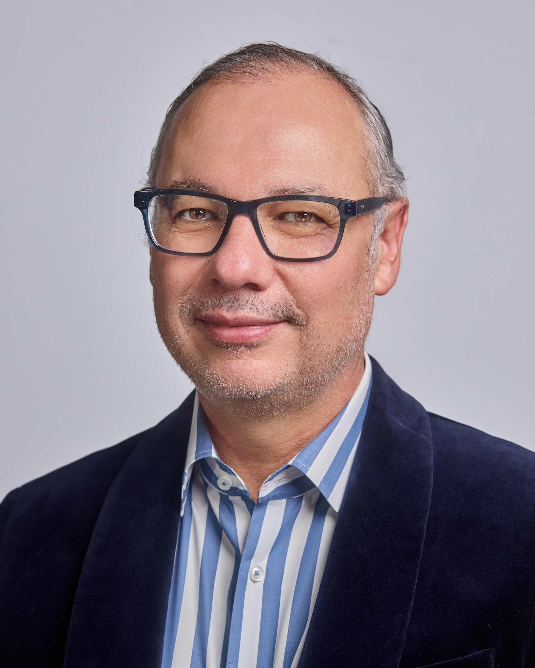 Studio headshot of a man in glasses and a navy blazer