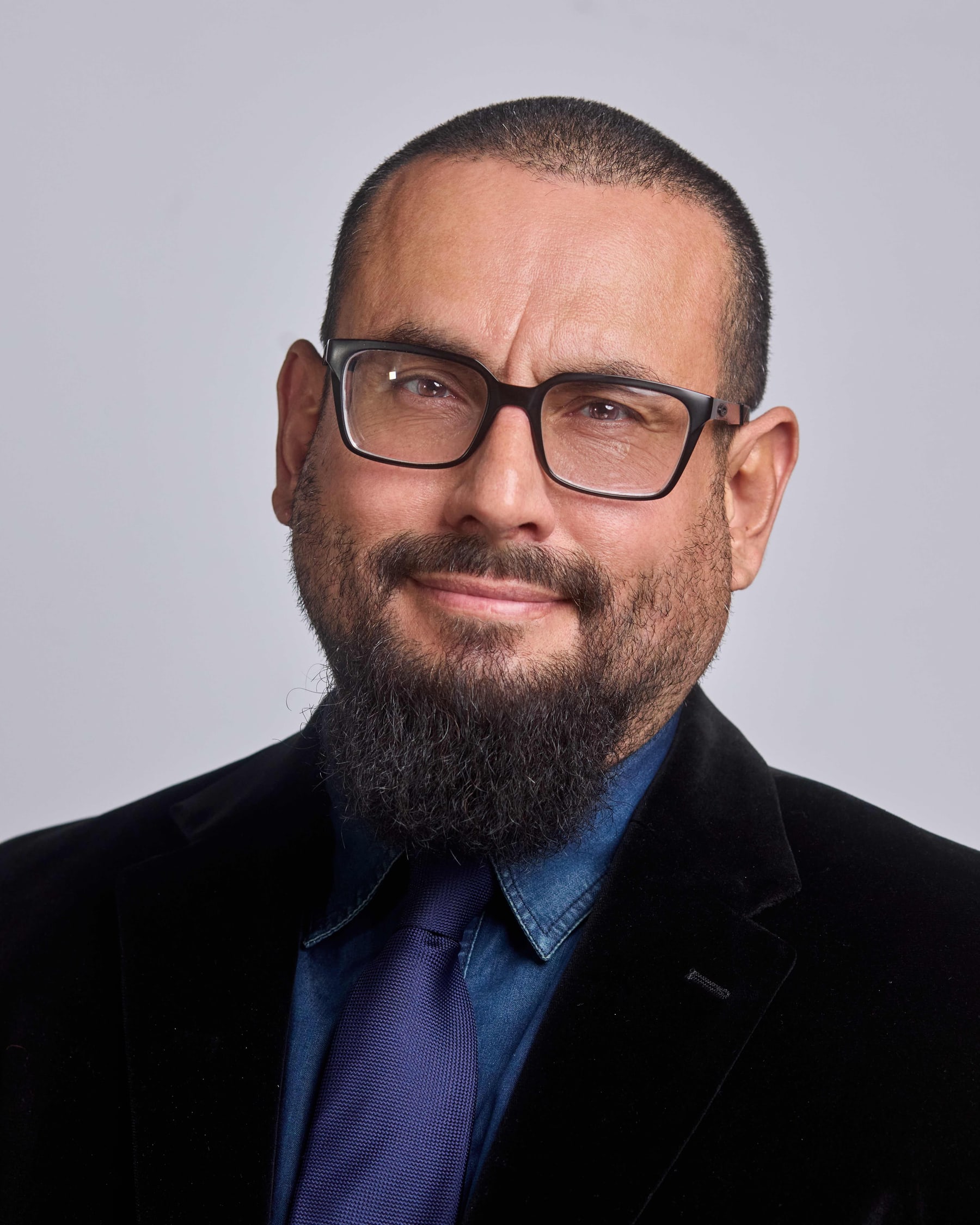 Studio headshot of a bearded man in glasses and a dark blazer