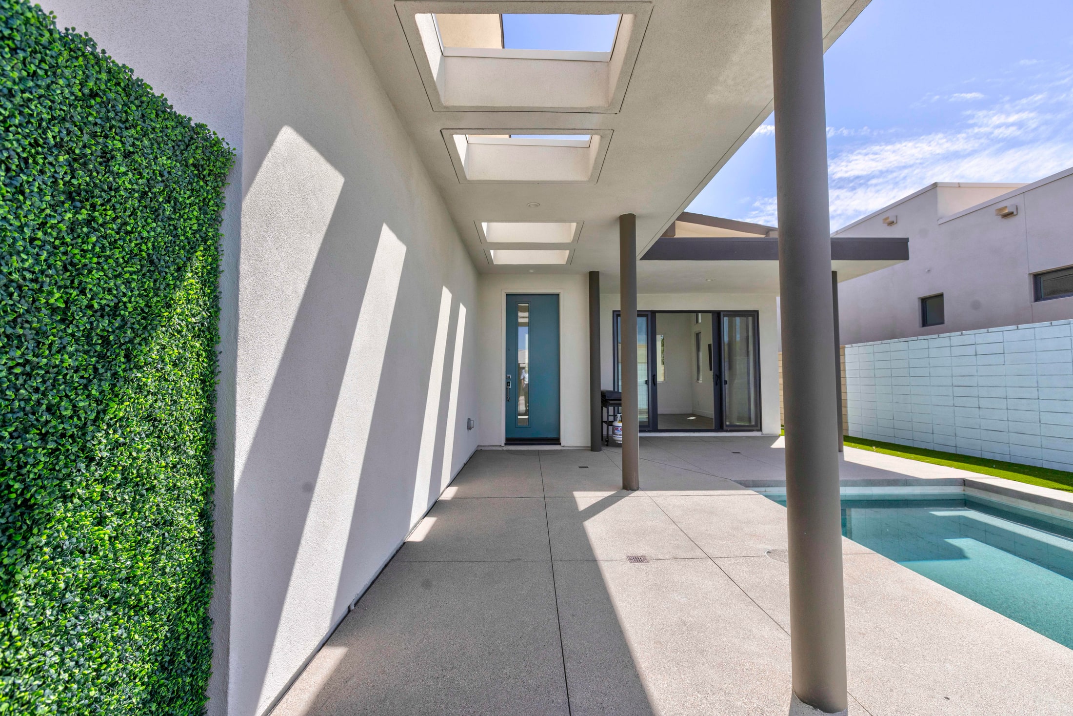Side walkway with a hedge and skylight beams looking through to the pool